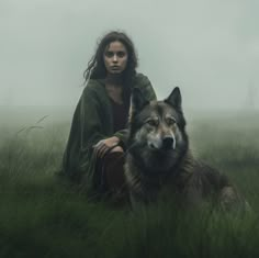 a woman sitting in the grass next to a wolf