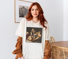 a woman standing in front of a table wearing a t - shirt with the painting's image on it