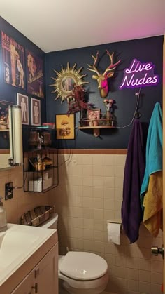 a bathroom with pictures on the wall and a neon sign above the toilette that says live nudees