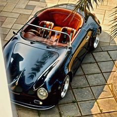 a black sports car parked on top of a brick sidewalk next to a palm tree