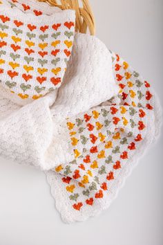 a white blanket with orange, yellow and green leaves on it next to a basket