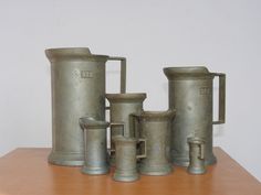 an assortment of old fashioned metal containers on a wooden table with white wall in the background