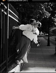 black and white photograph of two people kissing on a fence with trees in the background