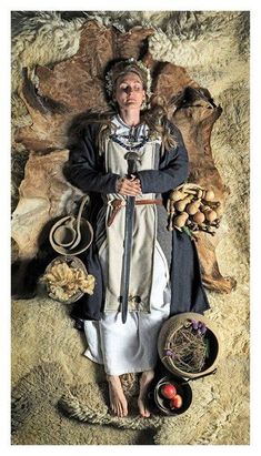 a woman dressed in medieval clothing standing next to some food and fruit on the ground