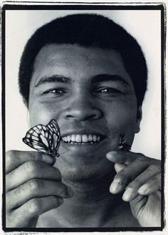 a black and white photo of a man with a butterfly on his nose looking at the camera