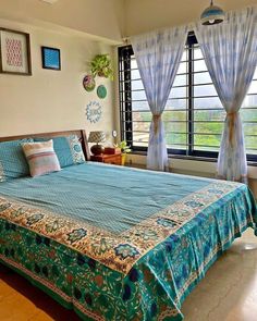 a large bed sitting in a bedroom next to a window covered in blue sheets and pillows