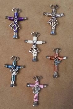 six different colored cross charms sitting on top of a brown paper covered surface with white and blue beads