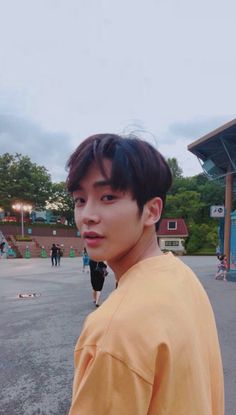 a young man standing in front of a basketball court wearing an orange shirt and looking at the camera