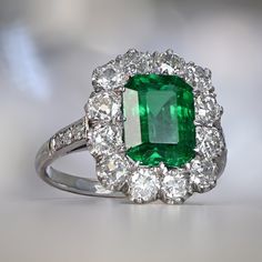 A rare and beautiful cluster ring that centers a natural emerald cut emerald weighing approximately 2.18-carat. Old European cut diamonds are arranged in a cluster around the central stone weighing approximately 1.50 carats in a low profile platinum ring. ✦ GEMSTONE SPECIFICATIONS: Center Gemstone: Emerald Center Gemstone Weight: Approx 2.18 Carats ✦ ENGAGEMENT RING SPECIFICATIONS: Total Diamond Weight: Approx 1.50 Carats Ring Material: Platinum ✦ WHAT COMES IN YOUR SHIPMENT: - Your Ring - Quali Cluster Green Emerald Ring In Platinum, Green Emerald Cluster Ring In Platinum, Platinum Cluster Emerald Ring, Green Platinum Emerald Ring With Cluster Shape, Emerald Cluster Ring With Gemstones, Classic Green Cluster Emerald Ring, Green Emerald Cluster Ring With Center Stone, Green Cluster Luxury Ring, Fine Jewelry Emerald Cluster Ring