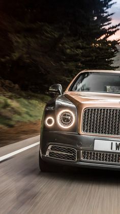 the front end of a brown car driving down a road