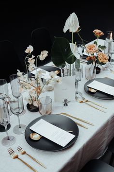 the table is set with black plates, silverware and white flowers in vases