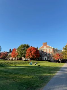 two people sitting on the grass in front of a large building with trees around it