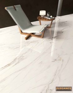 a white chair sitting on top of a marble floor next to a table with two glasses