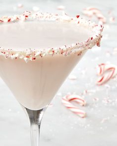 a drink in a martini glass with candy canes on the rim and white frosting