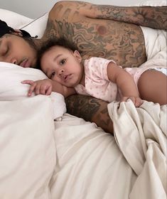 a woman and child laying on top of a bed next to each other with tattoos on their arms