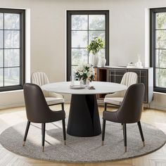 a round table with chairs around it in front of two windows and a potted plant