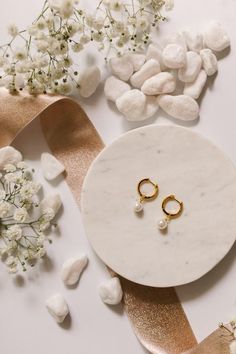 two pairs of earrings sitting on top of a marble table next to flowers and ribbon