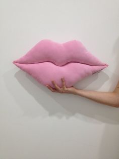 a person holding a pink pillow in the shape of a lips on a white wall