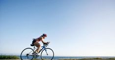 a woman is riding her bike on the road by the water and blue skies in the background