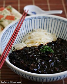 a bowl filled with noodles and black sauce next to chopsticks on a table