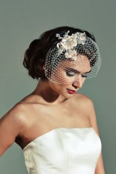 a woman in a wedding dress wearing a birdcage veil with flowers on it