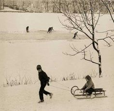 black and white photograph of two people pulling a sleigh in the snow with one person on it