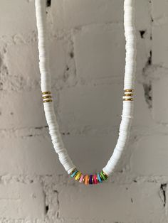 a white necklace with multi colored beads hanging from it's side on a brick wall