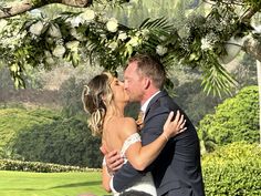 a bride and groom kissing under an outdoor wedding ceremony arch with greenery in the background