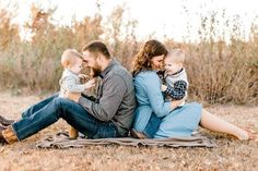 a man, woman and child sitting on a blanket in the middle of a field