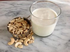 a glass of milk with cashews next to it on a marble counter top