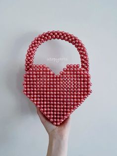 a hand holding a red beaded heart shaped purse on top of a white wall