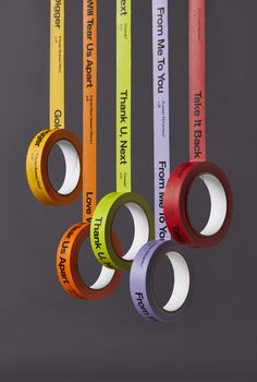 four rolls of colored tape hanging from the ceiling in front of a gray background with words on them