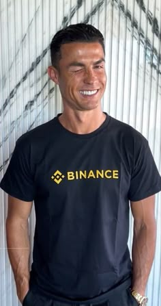 a man standing in front of a wall wearing a black shirt with the word binance on it