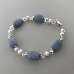 a blue bracelet with white pearls and crystal beads on a gray surface, the bead is attached to an adjustable clasp