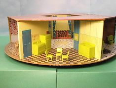 a doll house with yellow furniture and checkered flooring on the walls, in front of a green background