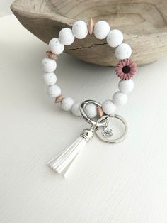 the white beaded bracelet has a tasseled charm with a flower on it