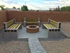 a fire pit surrounded by wooden benches in a graveled area next to a brick wall