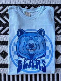 Get this popular new Bears Mascot shirt and show off your school spirit in style!  Each shirt is printed in-house by me using high-quality materials on a Comfort Colors shirt, known for its exceptional comfort, style, and durability. Even the glitter is printed! No need to worry about peeling glitter vinyl, or messy glitter flakes. Available in unisex sizes S to 3X, and youth sizes, we've got you covered regardless of your preferred fit. The Preppy Bears Shirt features a classic crew neck and short sleeves, making it suitable for year-round wear. The flattering silhouette ensures a comfortable and stylish fit for both men and women. Color shown: Chambray Note: As each shirt is individually printed, slight variations in color and placement may occur, adding to the uniqueness and charm of yo Team Spirit Sublimation Print Shirt For Streetwear, Team Spirit Sublimation Print Streetwear Shirt, Blue Graphic Print Shirt For Fan Gear, Blue Shirt With Graphic Print For Fan Gear, Blue Shirt With Graphic Print For Fans, Casual Blue Shirt For Fan Gear, Sports Fan Pre-shrunk Cotton Shirt, Blue Screen Print Shirt For College, Blue College Shirt With Screen Print