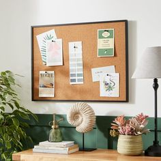 a cork board mounted to the side of a wall next to a lamp and potted plant