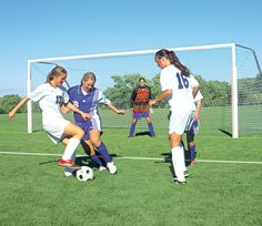 three girls are playing soccer on the field while one girl is trying to kick the ball