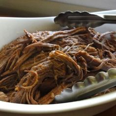 a white bowl filled with meat and two spoons