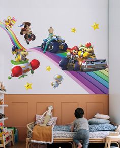 a child is sitting on a bed in front of a wall with mario kart and friends