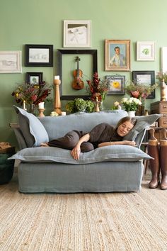 a woman laying on top of a couch in a living room next to framed pictures