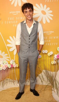 a young man in a gray suit and white shirt smiles at the camera while standing on a carpet