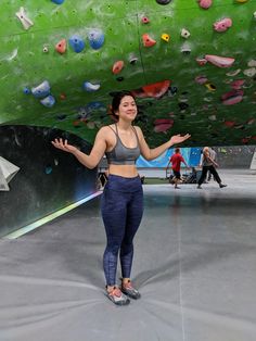 a woman standing in front of a climbing wall with her hands out to the side