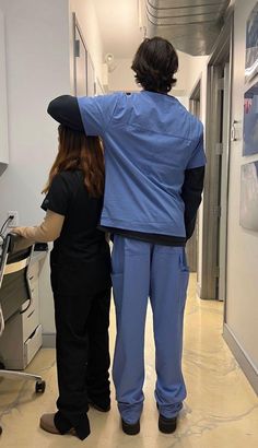 two people in scrubs standing next to each other looking at something on the wall