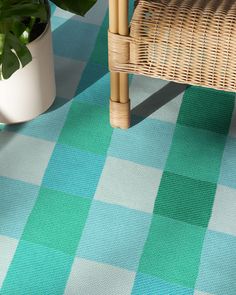 a wicker chair sitting on top of a blue and green checkered rug next to a potted plant