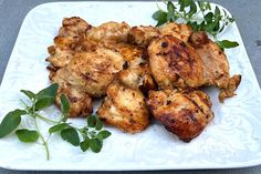 grilled chicken on a white plate with green garnishes and leaves around it