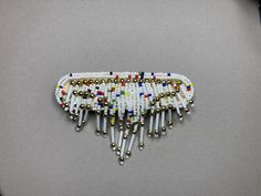 a white beaded brooch with multicolored beads and metal bells on it