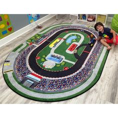 a young boy sitting on the floor in front of a rug with cars and trucks